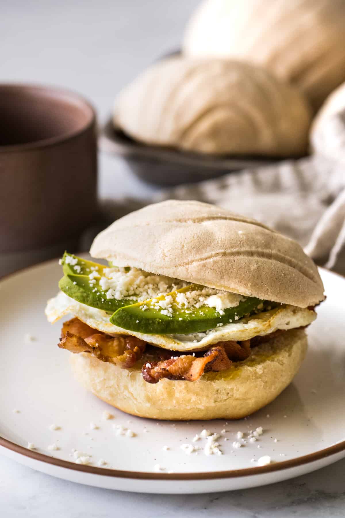 A concha breakfast sandwich on a plate with a cup of coffee in the background.