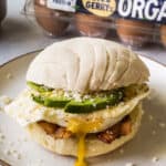 A concha breakfast sandwich on a plate made from bacon, a fried egg, avocado, cotija cheese, and a maple conchas.