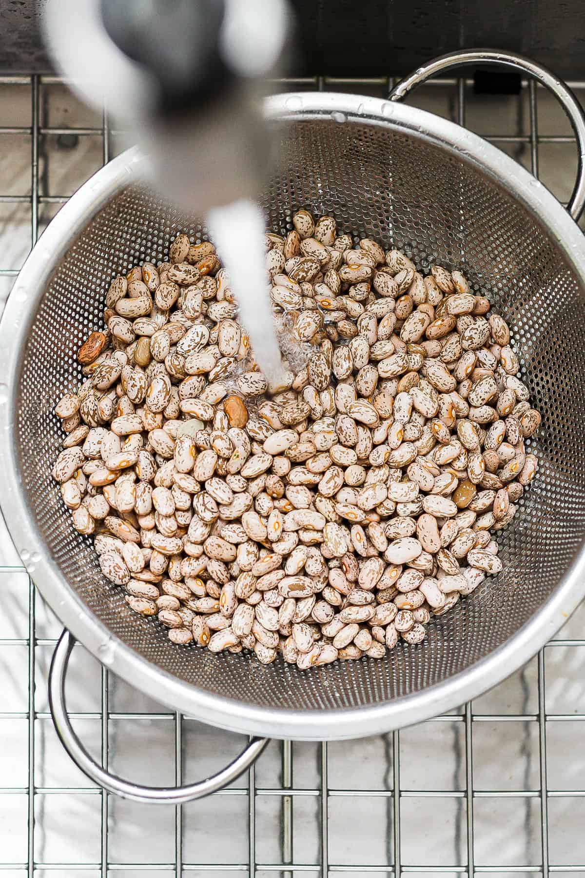 Pinto beans being rinsed in a strainer.