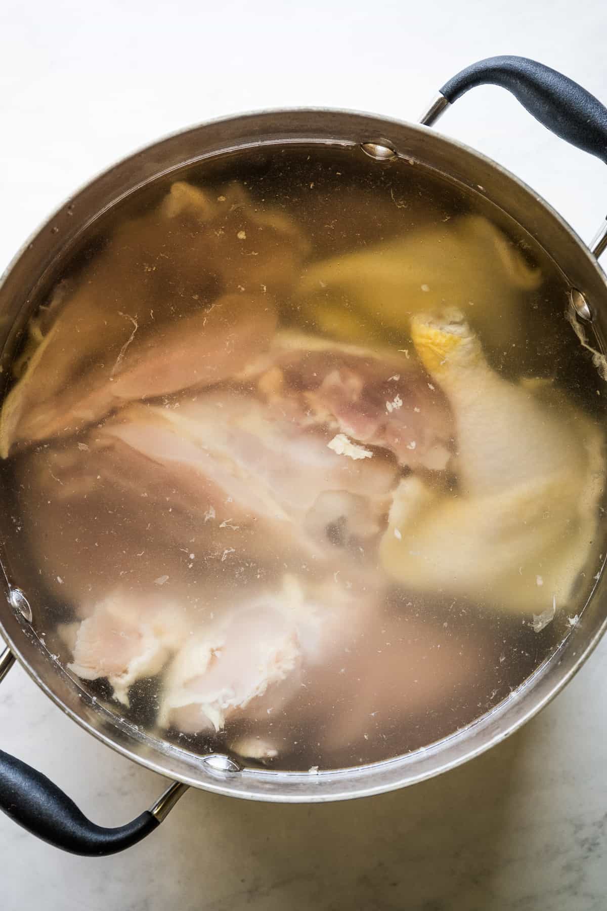 A whole chicken boiling in a pot covered covered with water.