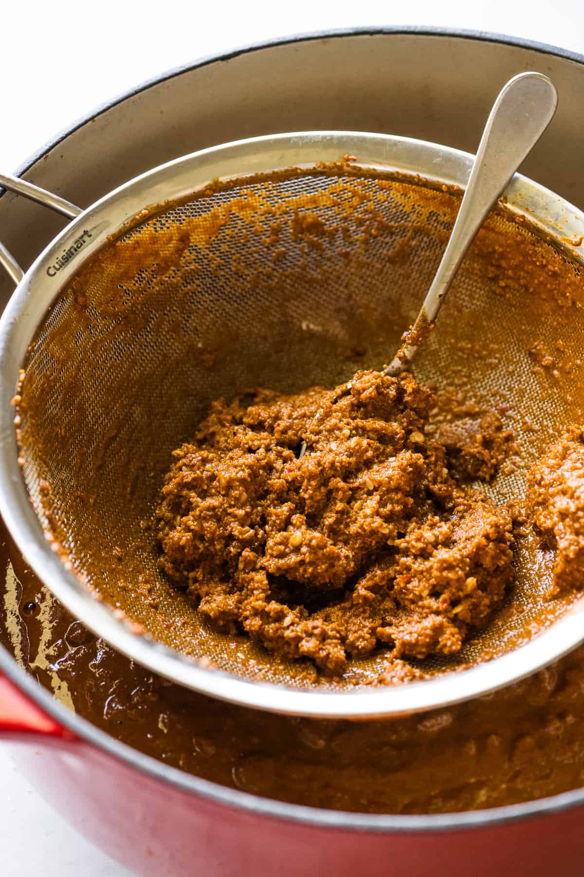 Mole sauce being strained into a large pot.