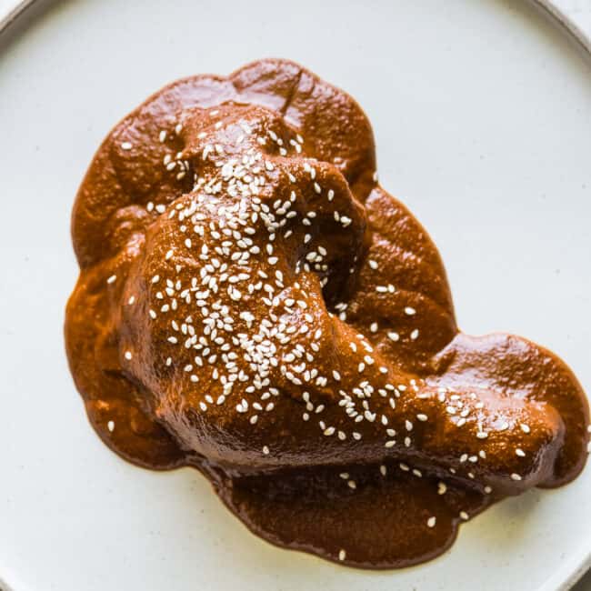 Mole sauce, or mole poblano, on a chicken leg and garnished with sesame seeds.