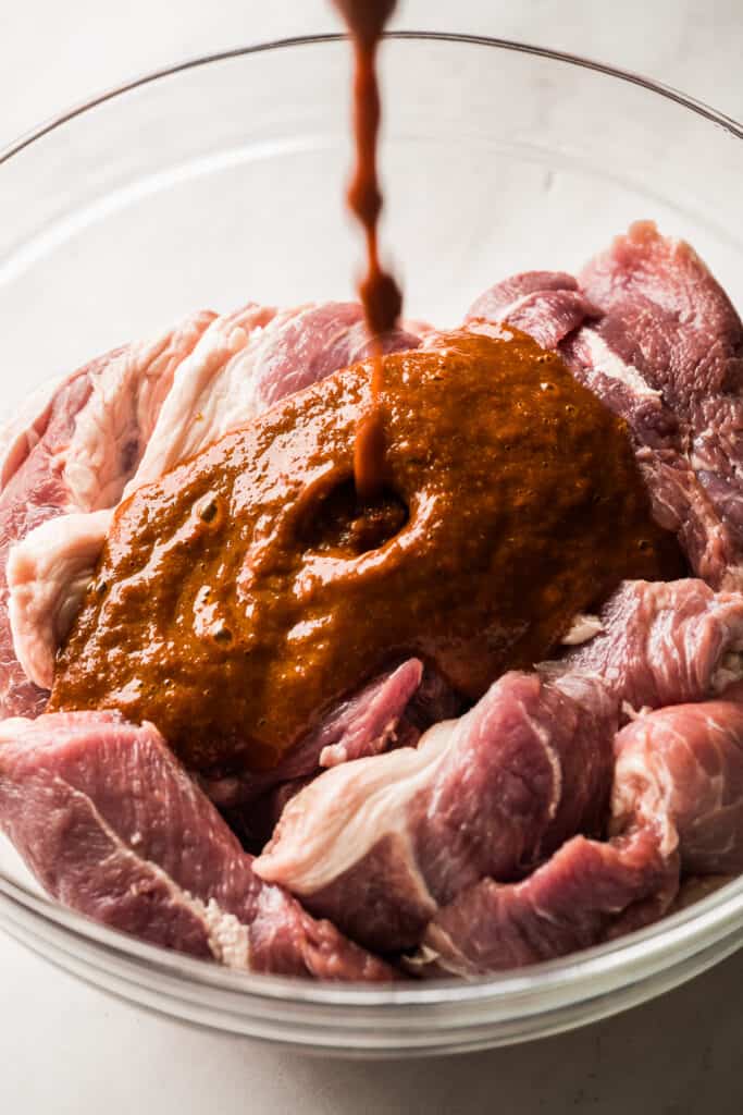 Marinade being poured into a glass bowl with pork shoulder.