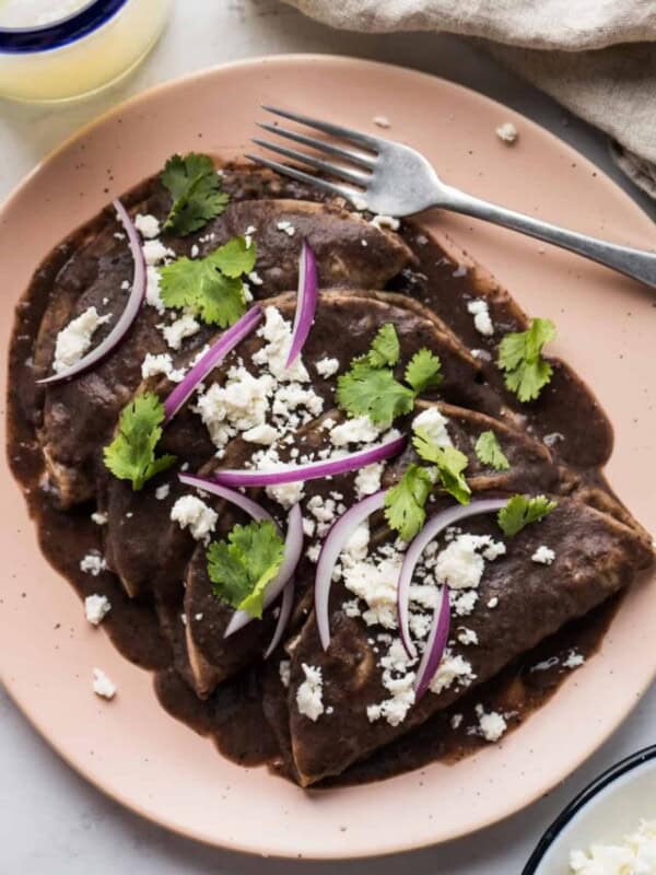Enfrijoladas covered in a blended bean sauce and garnished with queso fresco, cilantro, and sliced onions.