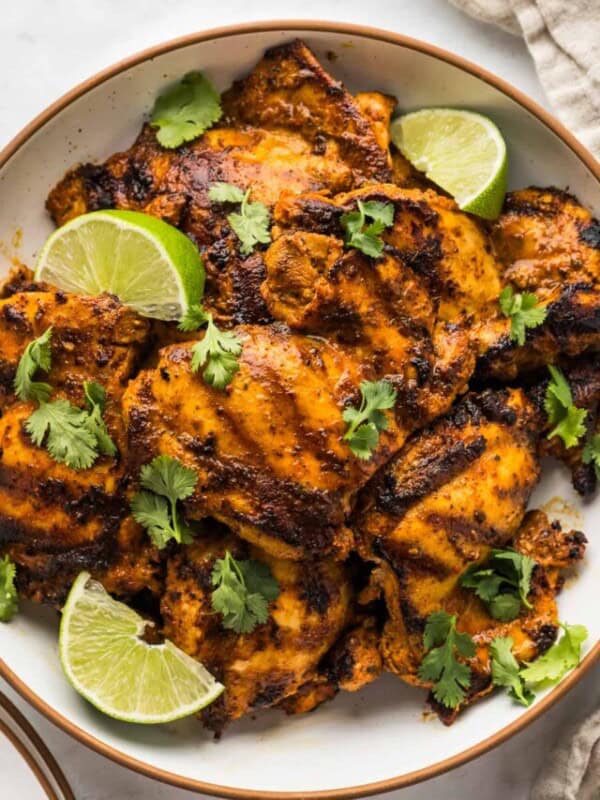 Grilled pollo asado on a serving plate garnished with cilantro and lime wedges.