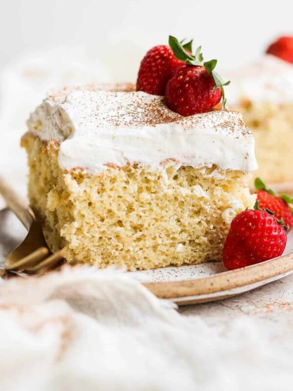 A slice of tres leches cake on a plate topped with whipped cream and fresh strawberries.