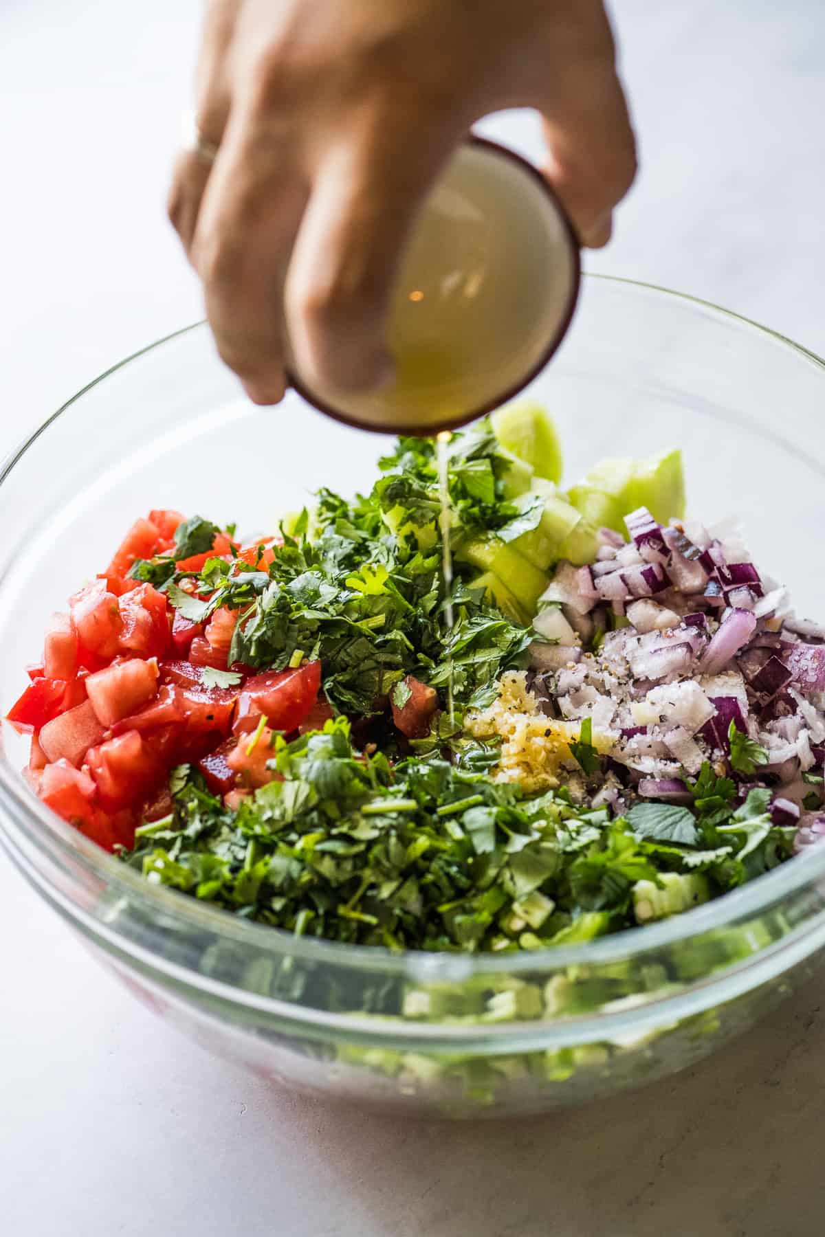 Olive oil being poured into a bowl of ingredients for cucumber salsa.