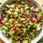 Cucumber Salsa in a bowl with tortilla chips, lime wedges, and cilantro on the side.