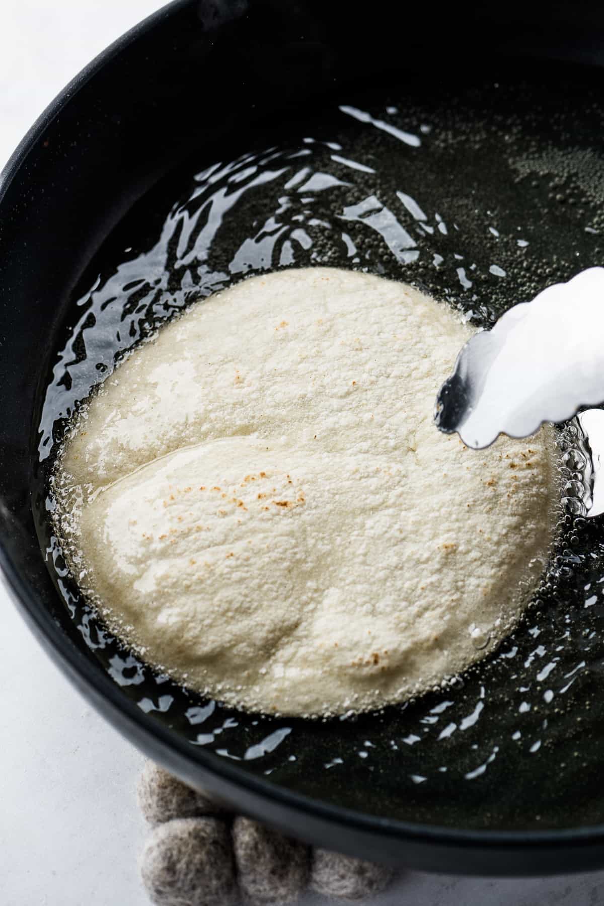 A corn tortilla frying in a skillet of oil.