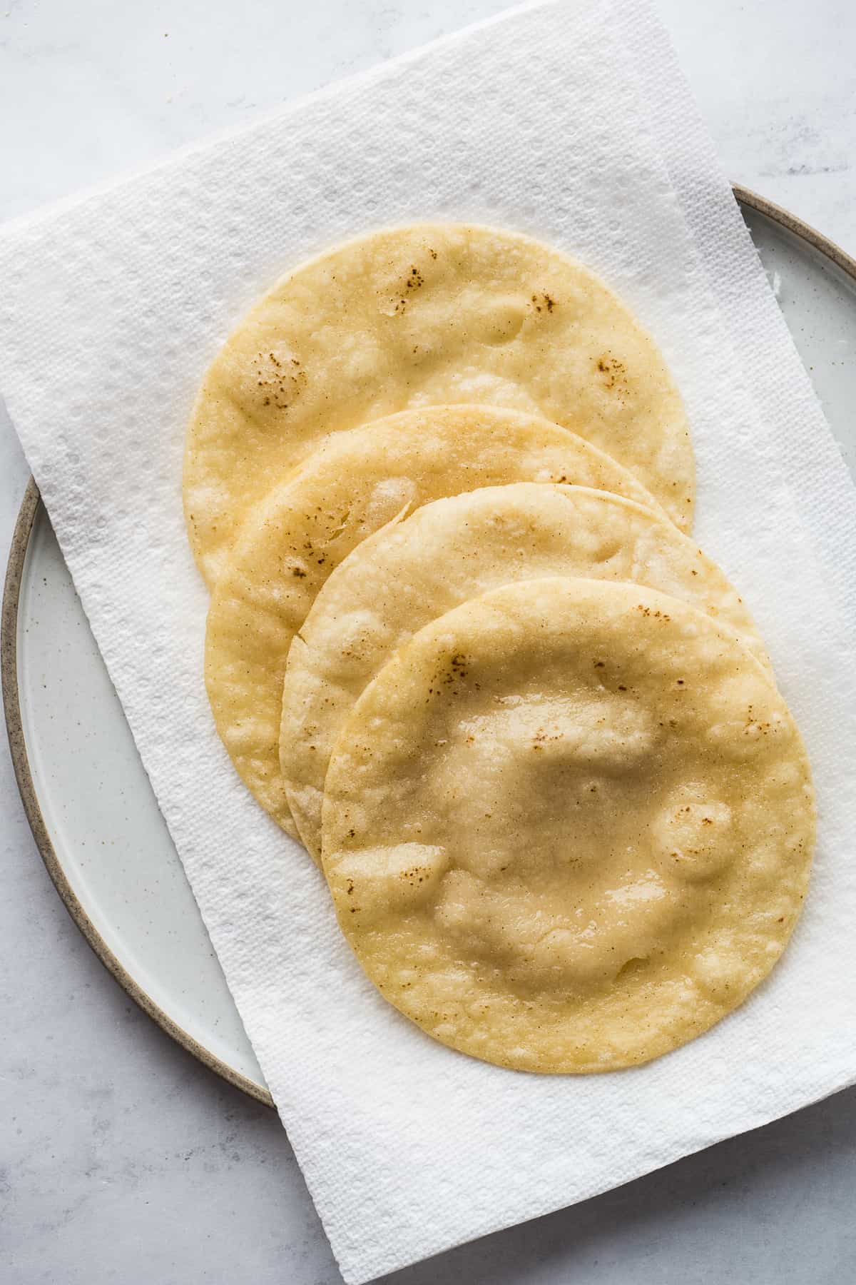 Lightly fried corn tortillas resting on a plate lined with paper towels.