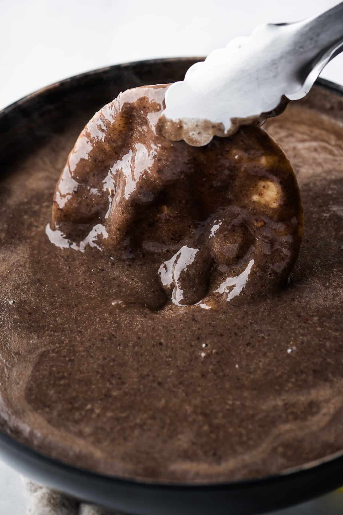 A corn tortilla being dipped in a black bean sauce.