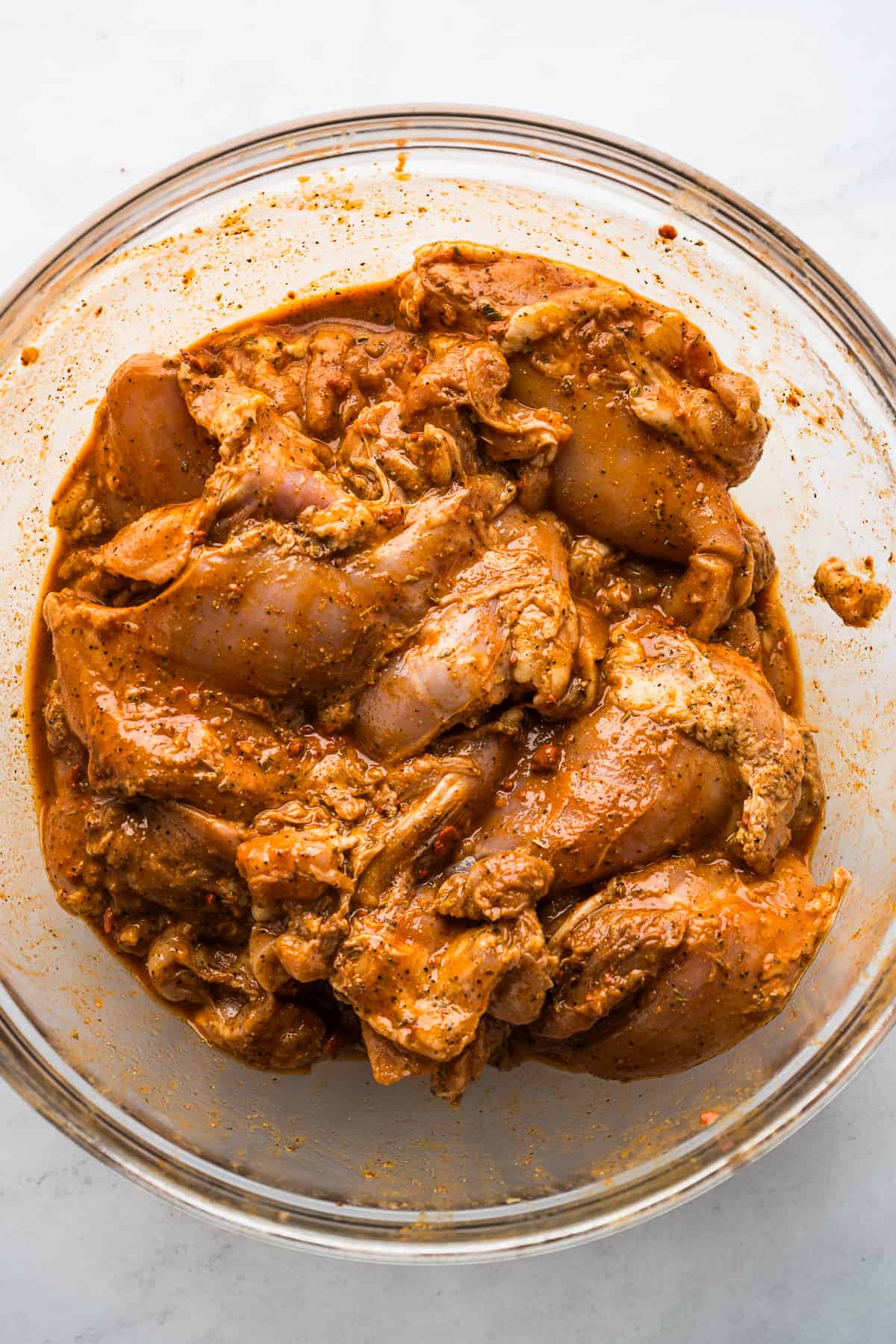 Boneless skinless chicken thighs marinating in pollo asado marinade in a glass bowl.