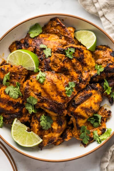 Grilled pollo asado on a serving plate garnished with cilantro and lime wedges.