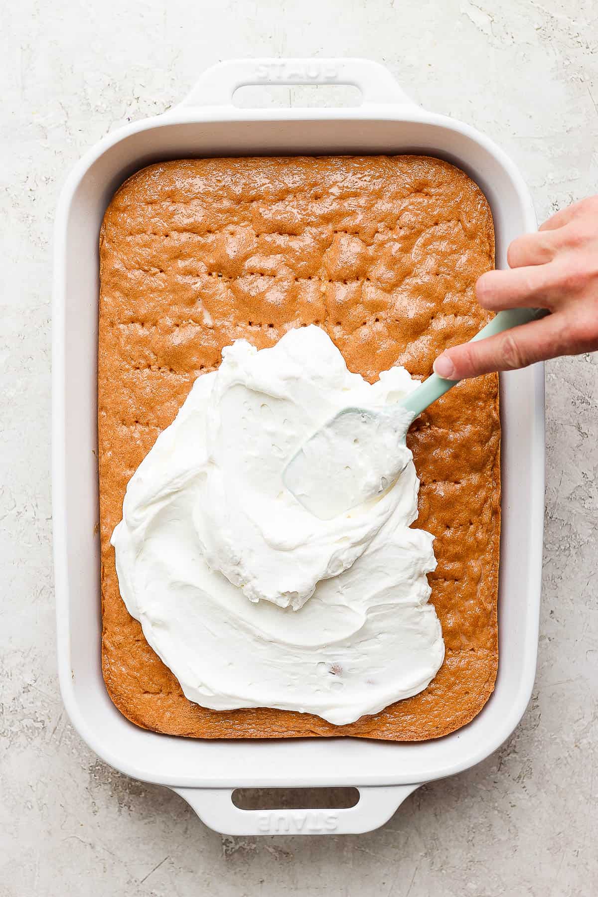 Whipped cream being spread on top of a tres leches cake.