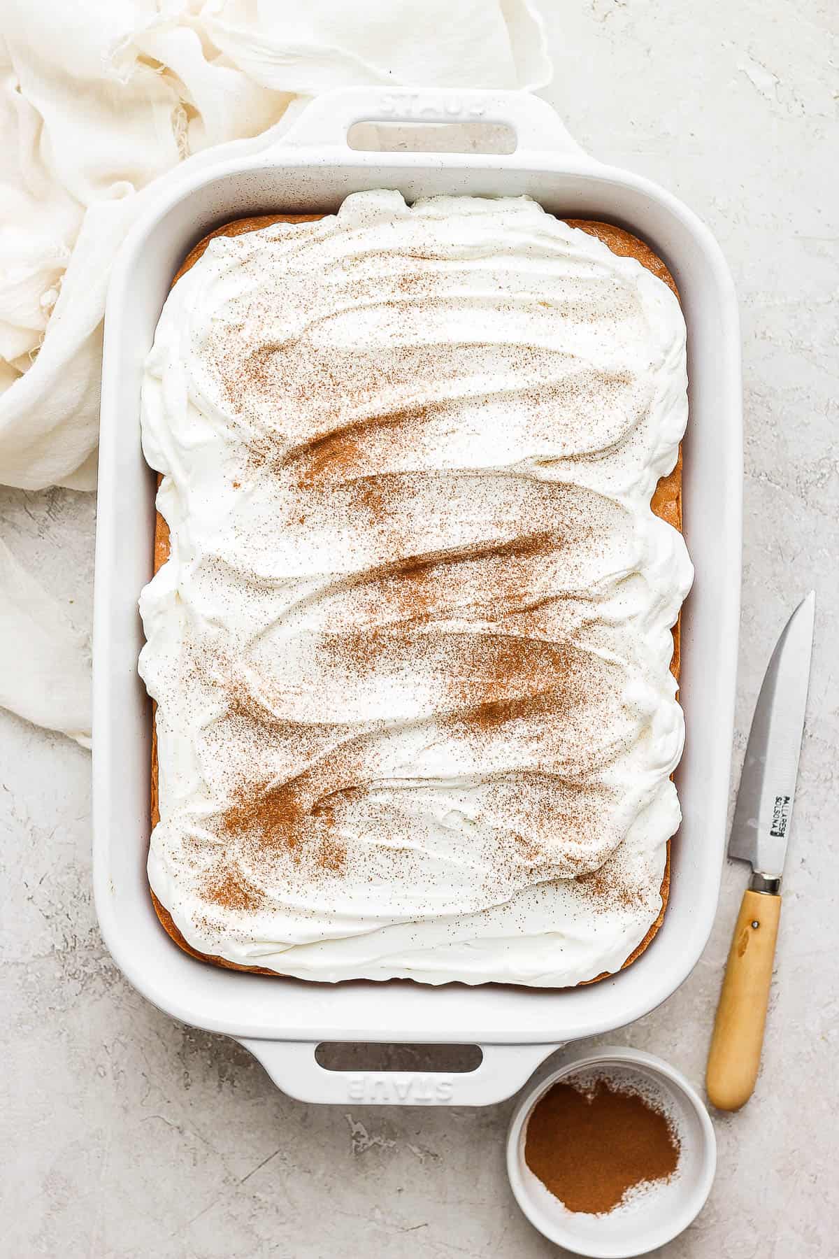 Tres leches cake in a baking pan topped with whipped cream and a sprinkle of ground cinnamon.