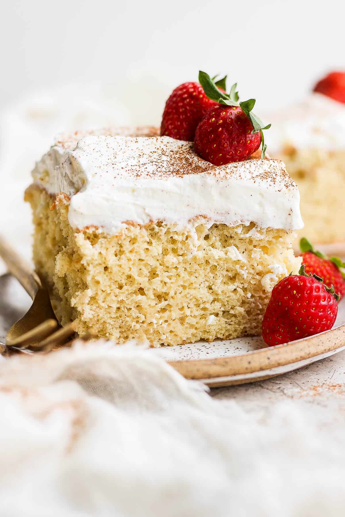 A slice of tres leches cake on a plate topped with whipped cream and fresh strawberries.