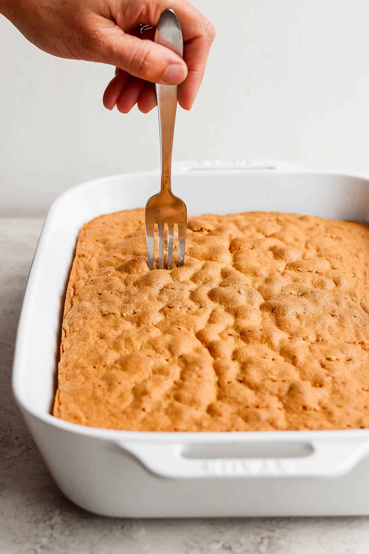 A fork poking holes all over a sponge cake to make tres leches cake.