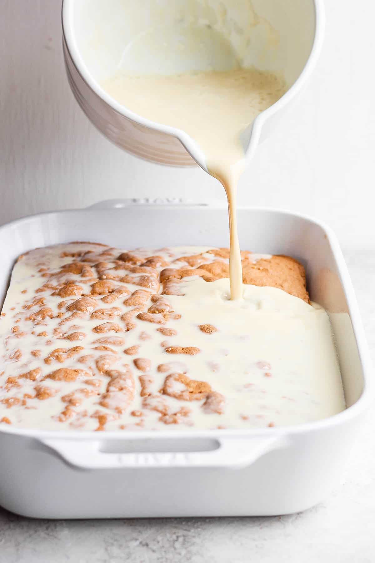 The three-milk mixture being poured all over the poked sponge of the tres leches cake.