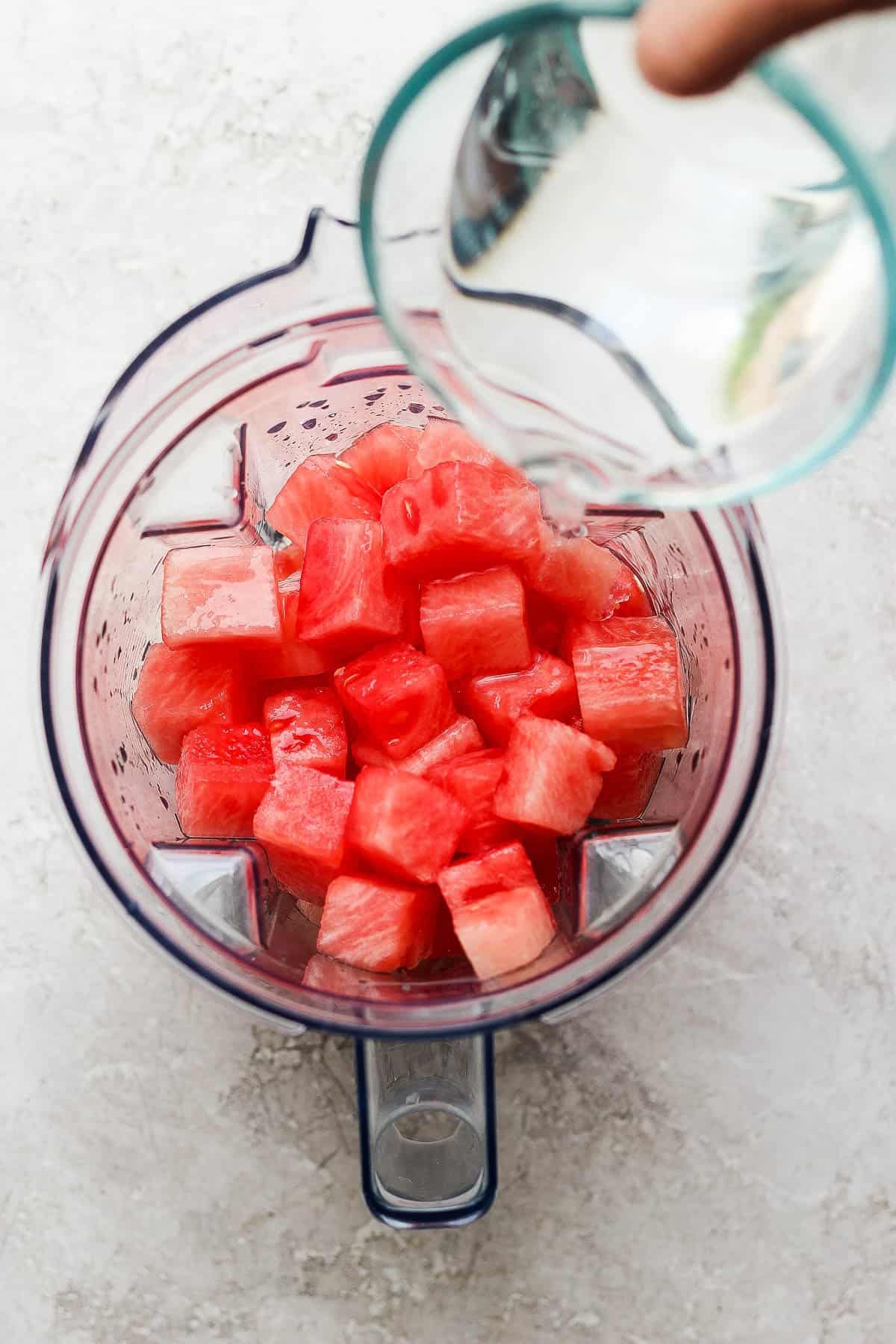 Water being poured into a blender with diced watermelon in it.