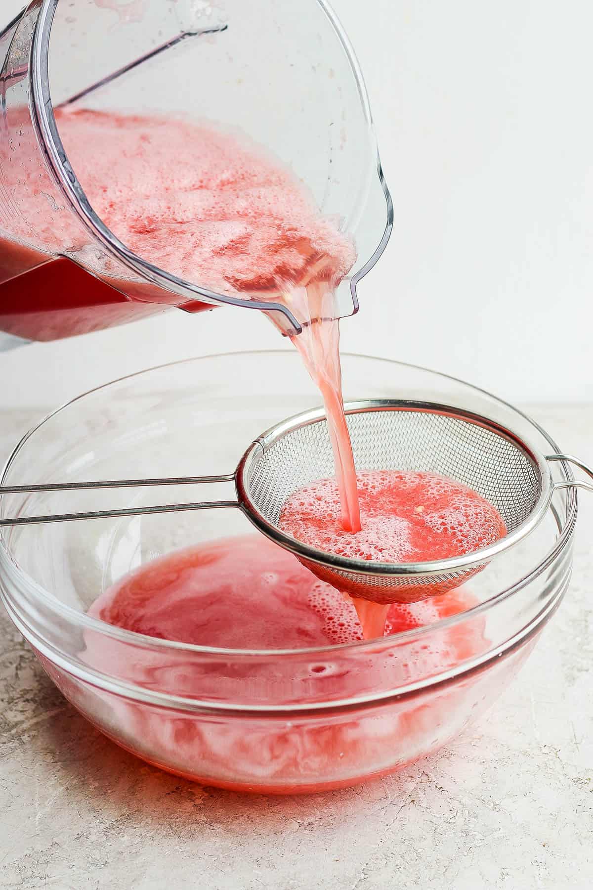 Watermelon agua fresca being poured through a strainer.