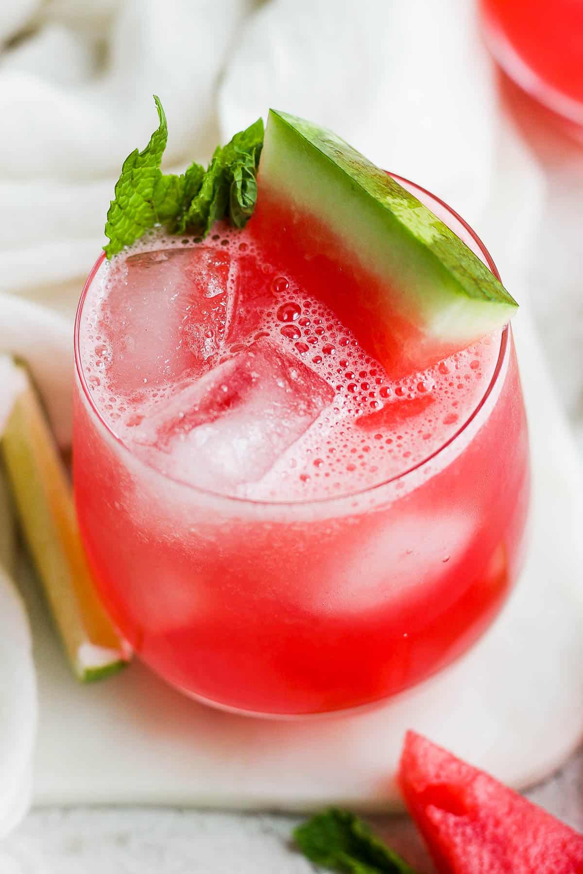 A glass of iced watermelon agua fresca (also known as agua de sandia) with a garnish of mint and fresh watermelon.