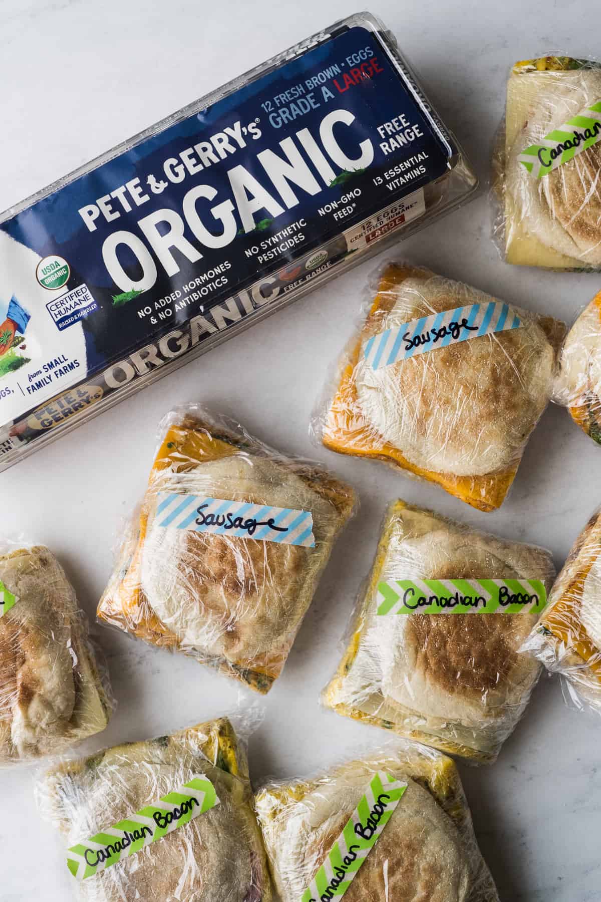 Breakfast sandwiches wrapped in plastic wrap and labeled on a table.