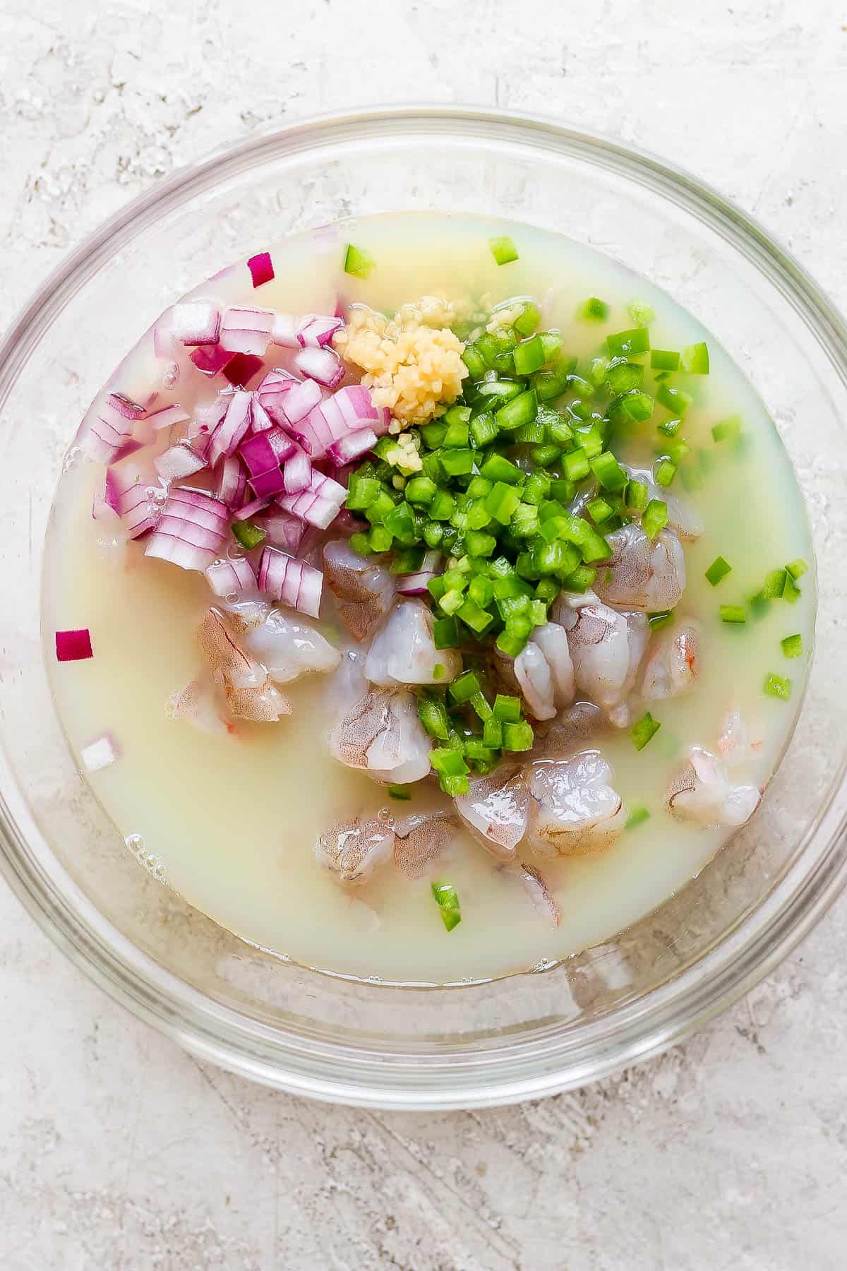 Lemon juice, lime juice, red onion, garlic, jalapeño, and shrimp in a bowl.