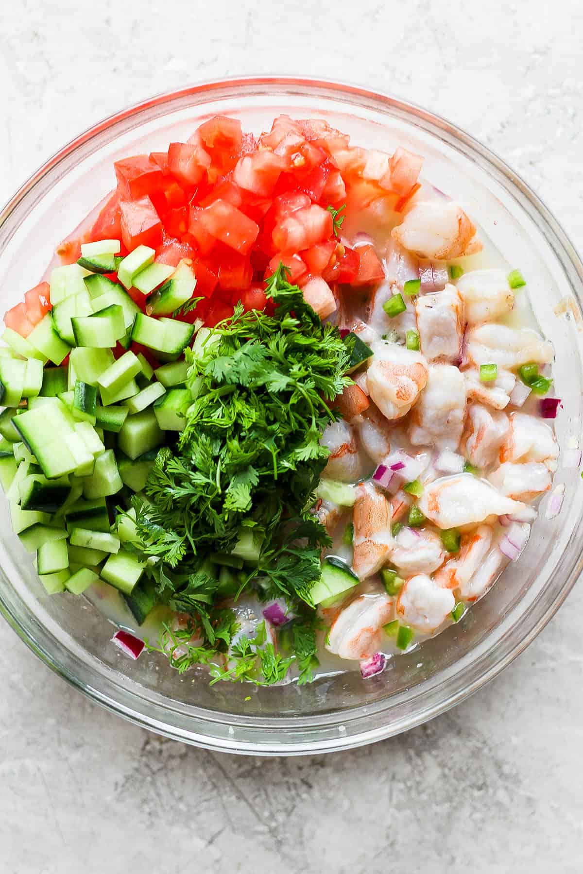 Cilantro, cucumber, tomato, and shrimp in a bowl of ceviche.