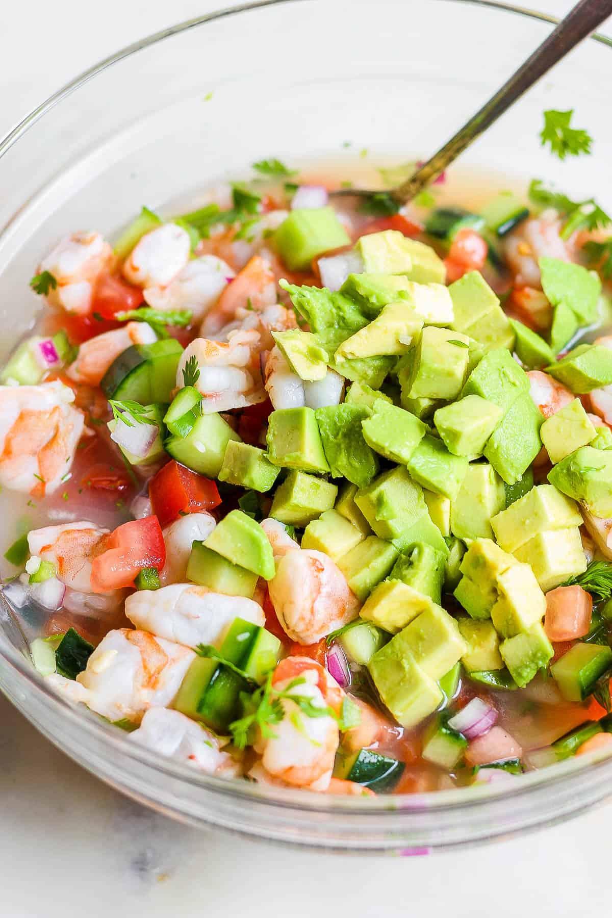 Avocado being mixed into a bowl of ceviche.
