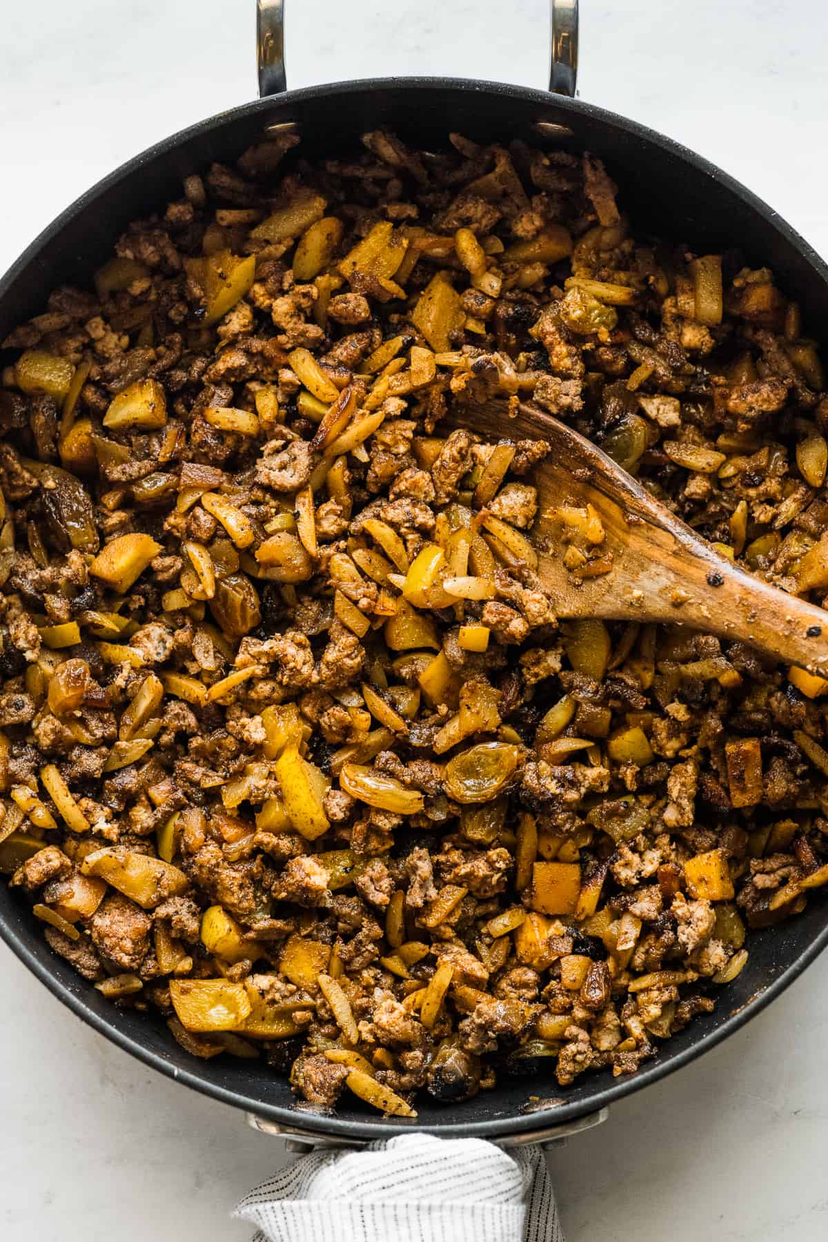 The cooked filling for chiles en nogada made from dried fruits, ground beef, and ground pork in a skillet.