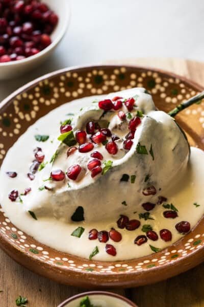 A chile en nogada on a plate garnished with pomegranate seeds and parsley.