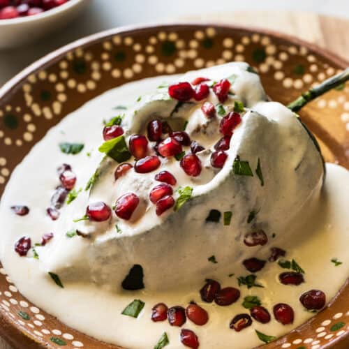 A chile en nogada on a plate garnished with pomegranate seeds and parsley.