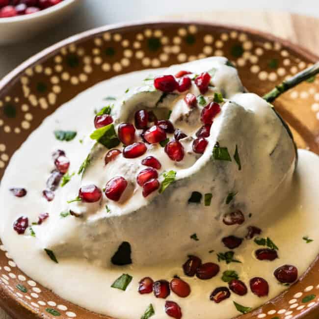 A chile en nogada on a plate garnished with pomegranate seeds and parsley.
