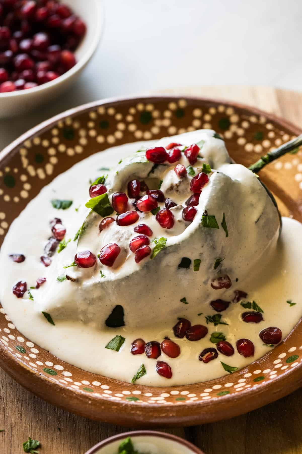 A chile en nogada on a plate garnished with pomegranate seeds and parsley.
