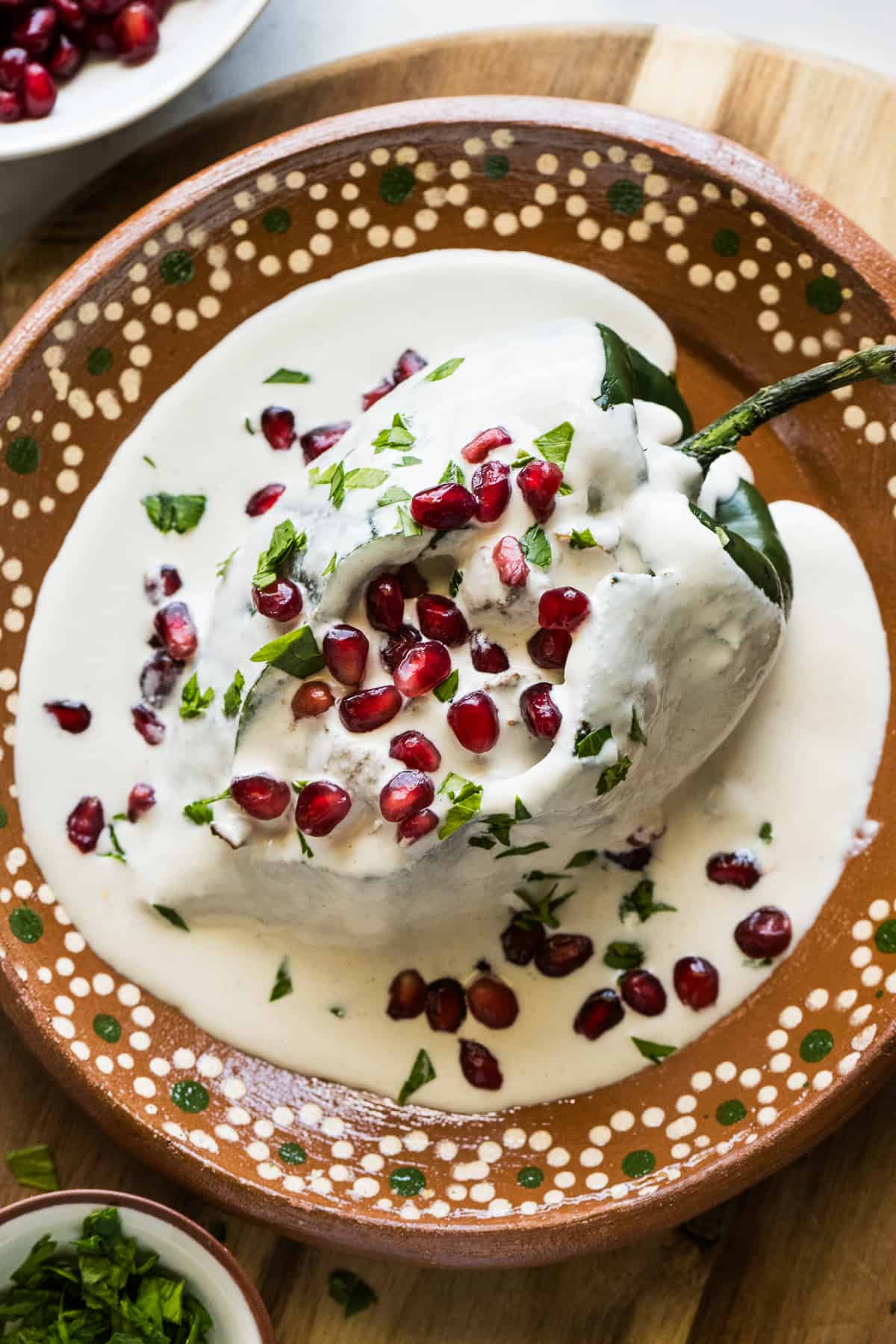 Mexican chiles en nogada topped with a walnut sauce and garnished with pomegranate seeds and chopped parsley.