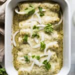 Enchiladas Suizas in a baking dish garnished with onions and cilantro.