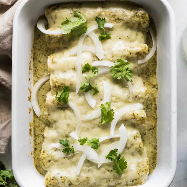 Enchiladas Suizas in a baking dish garnished with onions and cilantro.