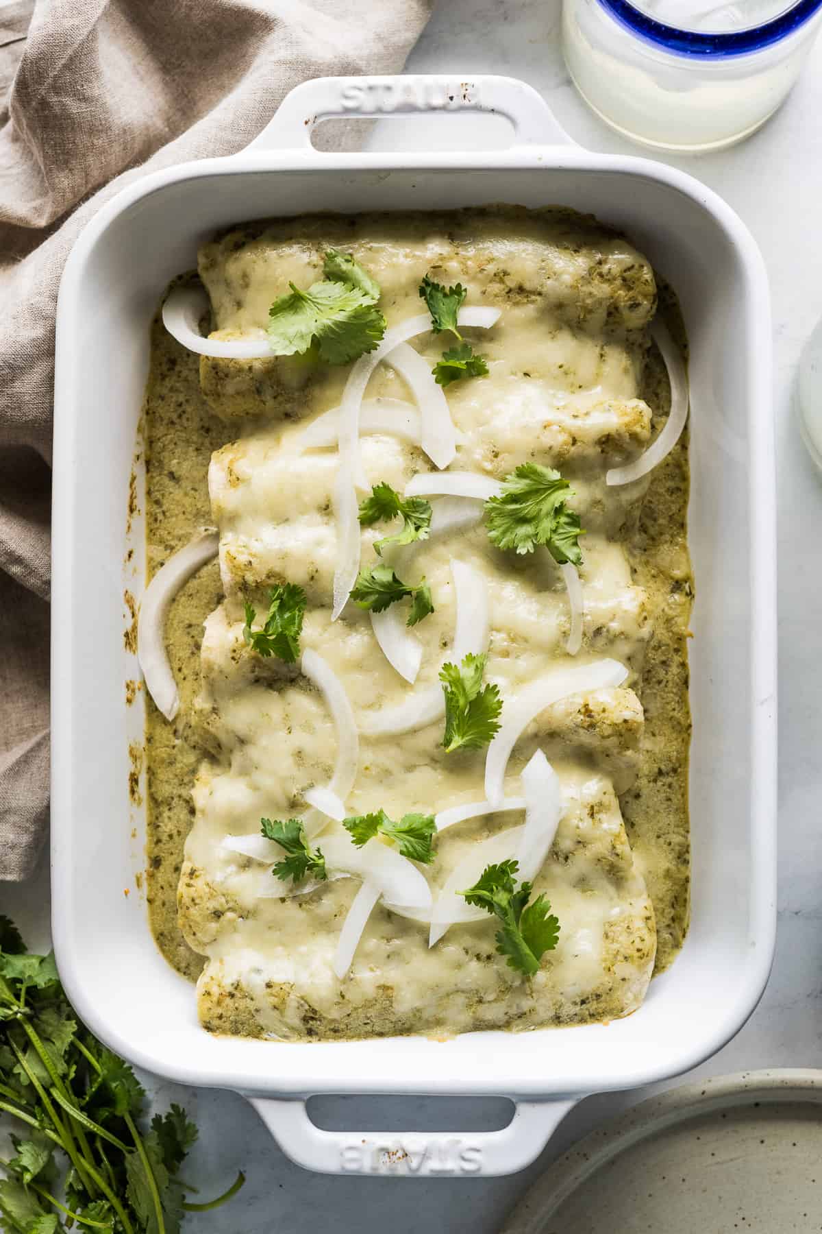 Enchiladas Suizas in a baking dish garnished with onions and cilantro.