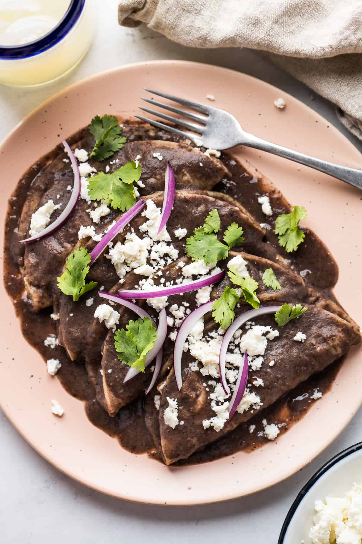 Enfrijoladas covered in a blended bean sauce and garnished with queso fresco, cilantro, and sliced onions.