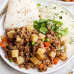Mexican picadillo on a plate with rice and flour tortillas.