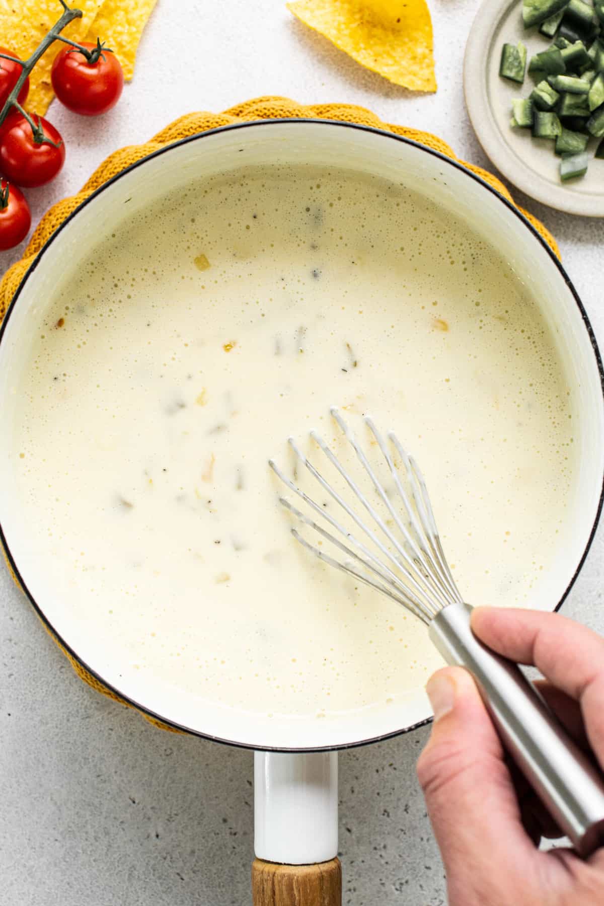 A whisk stirring a pot of melted queso blanco.