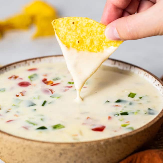 A bowl of queso blanco with a tortilla chip being dipped into it.