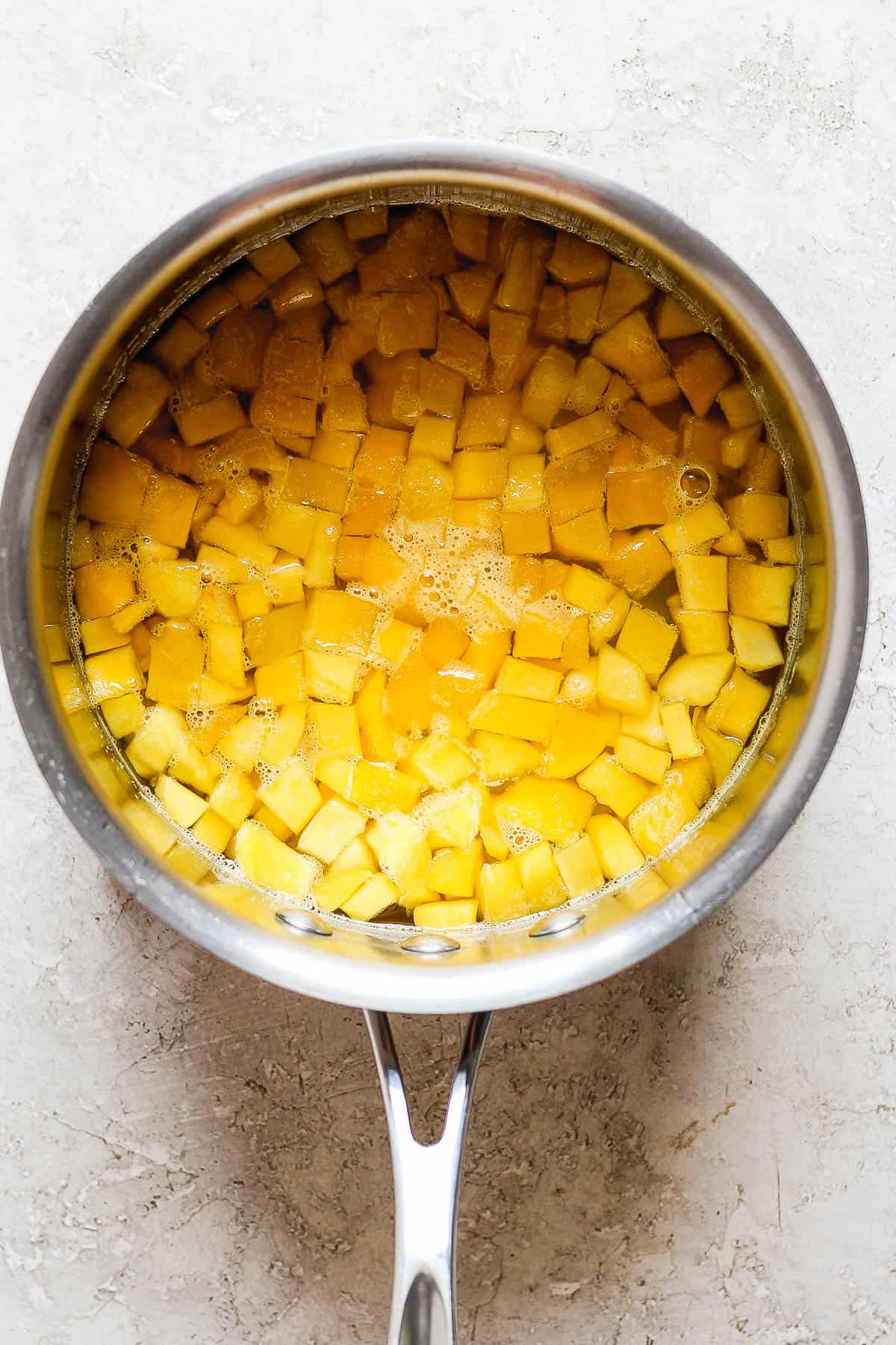 Diced mango in a saucepan with water and sugar to create a syrup for raspados.