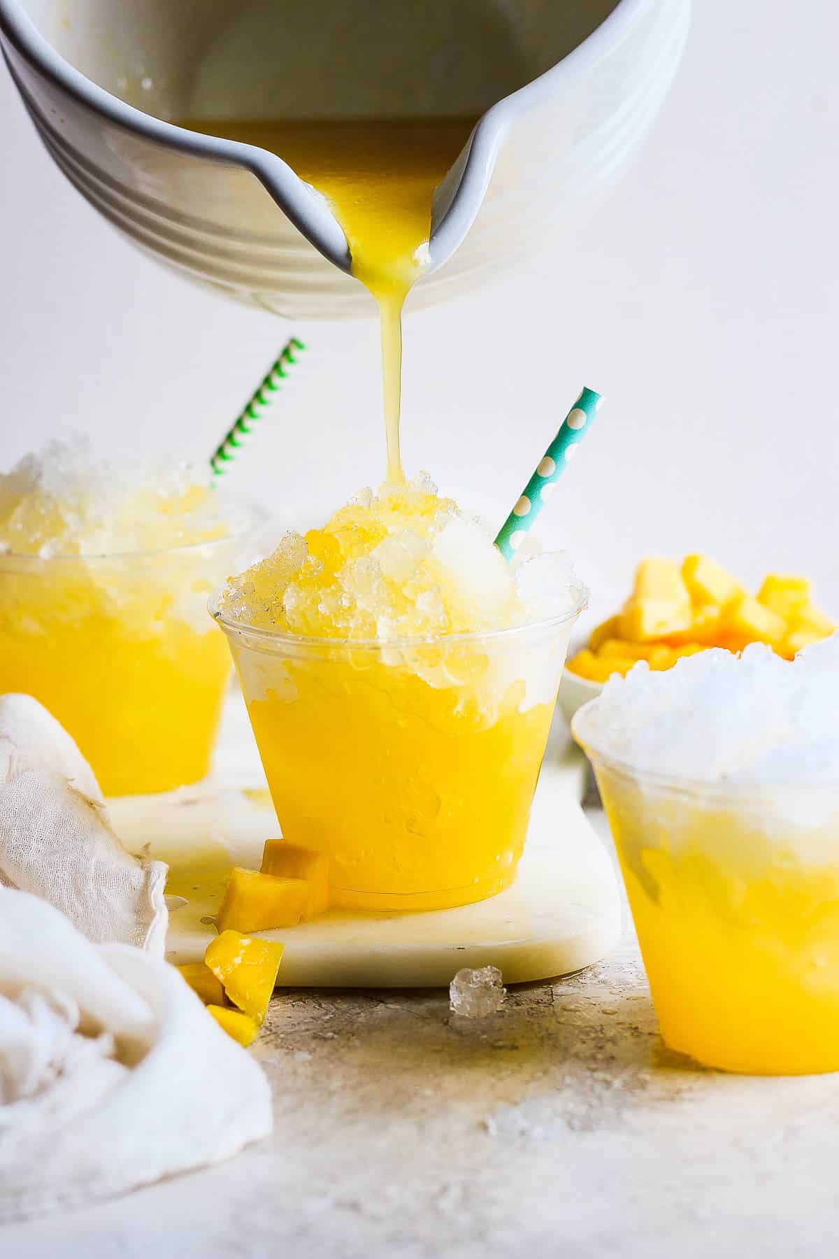 Raspados in a plastic cup with mango syrup being poured on top