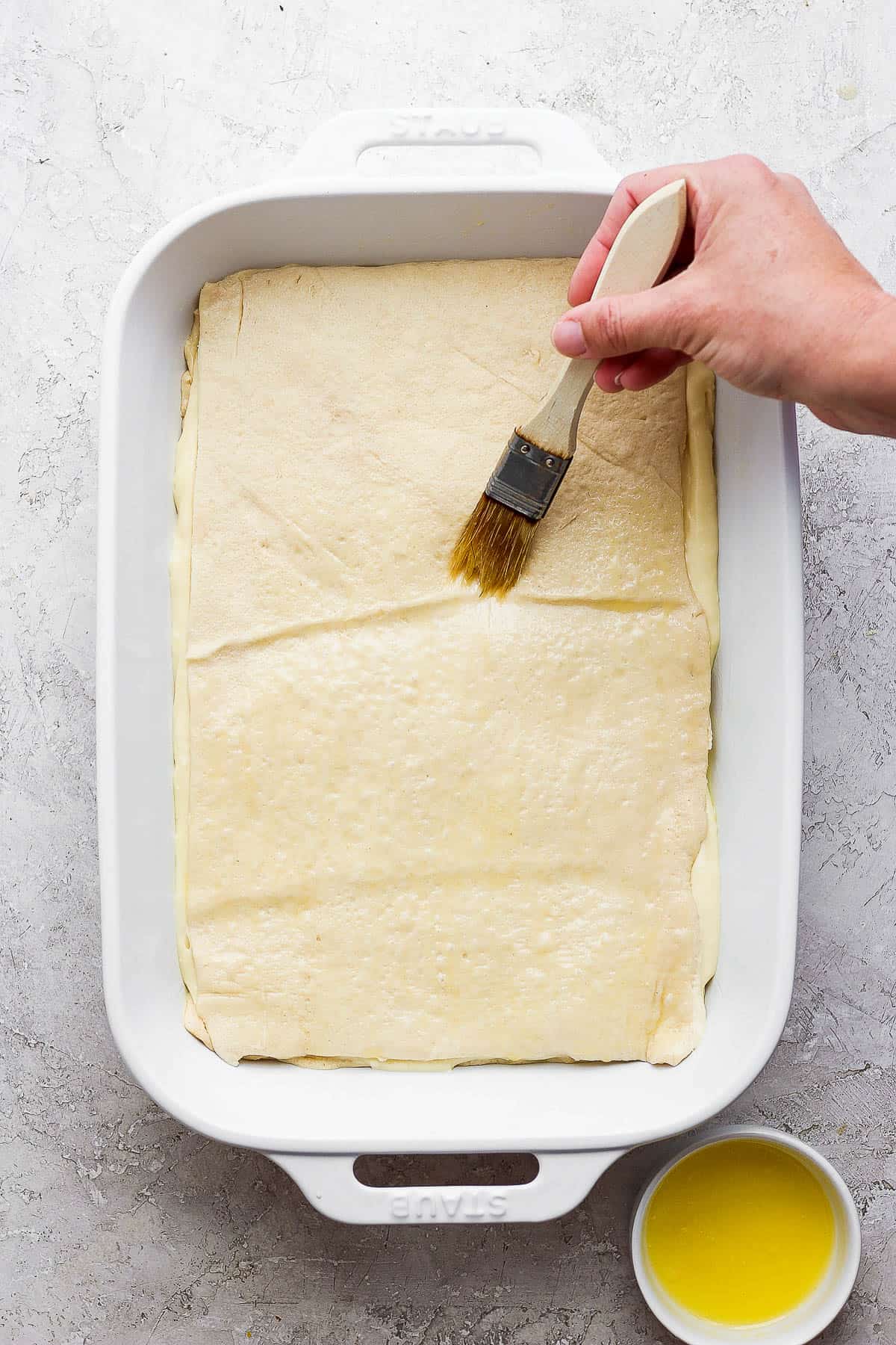 Brushing melted butter on top of crescent roll dough.