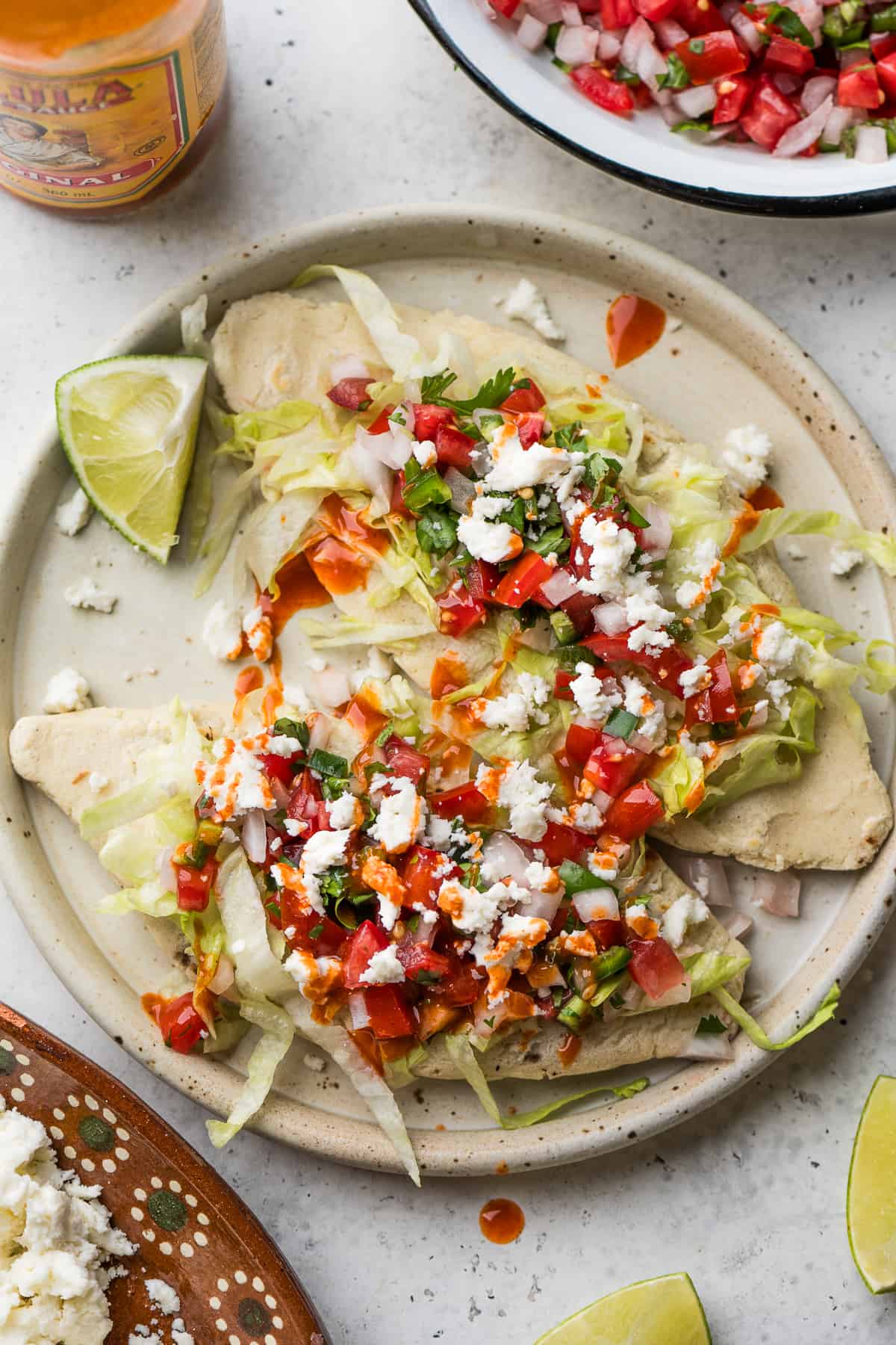 Tlacoyos topped with salsa, queso fresco, pico de gallo, and lettuce.