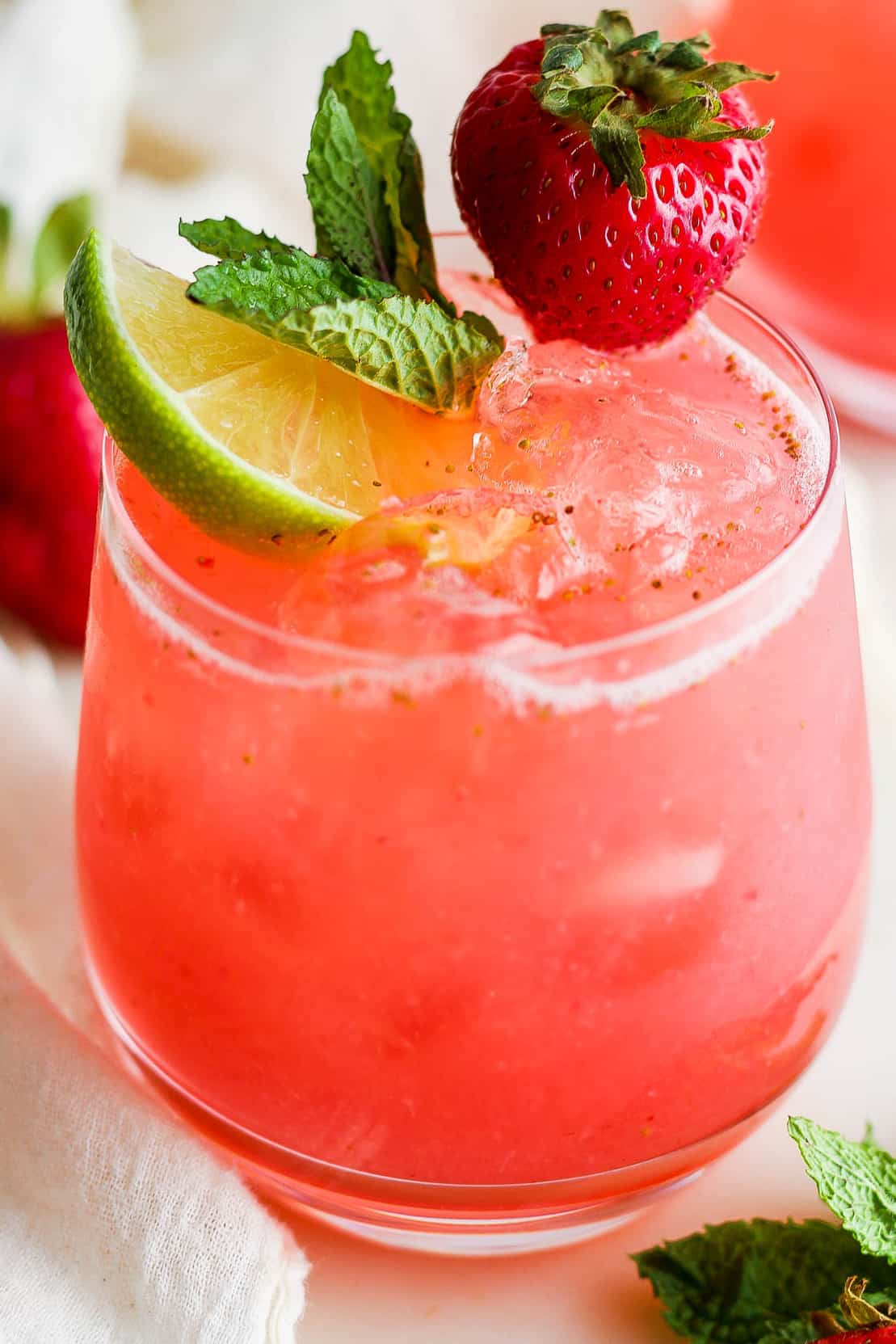Agua de Fresa (strawberry agua fresca) in a glass with ice and garnished with a lime wedge, a mint sprig, and a fresh strawberry.