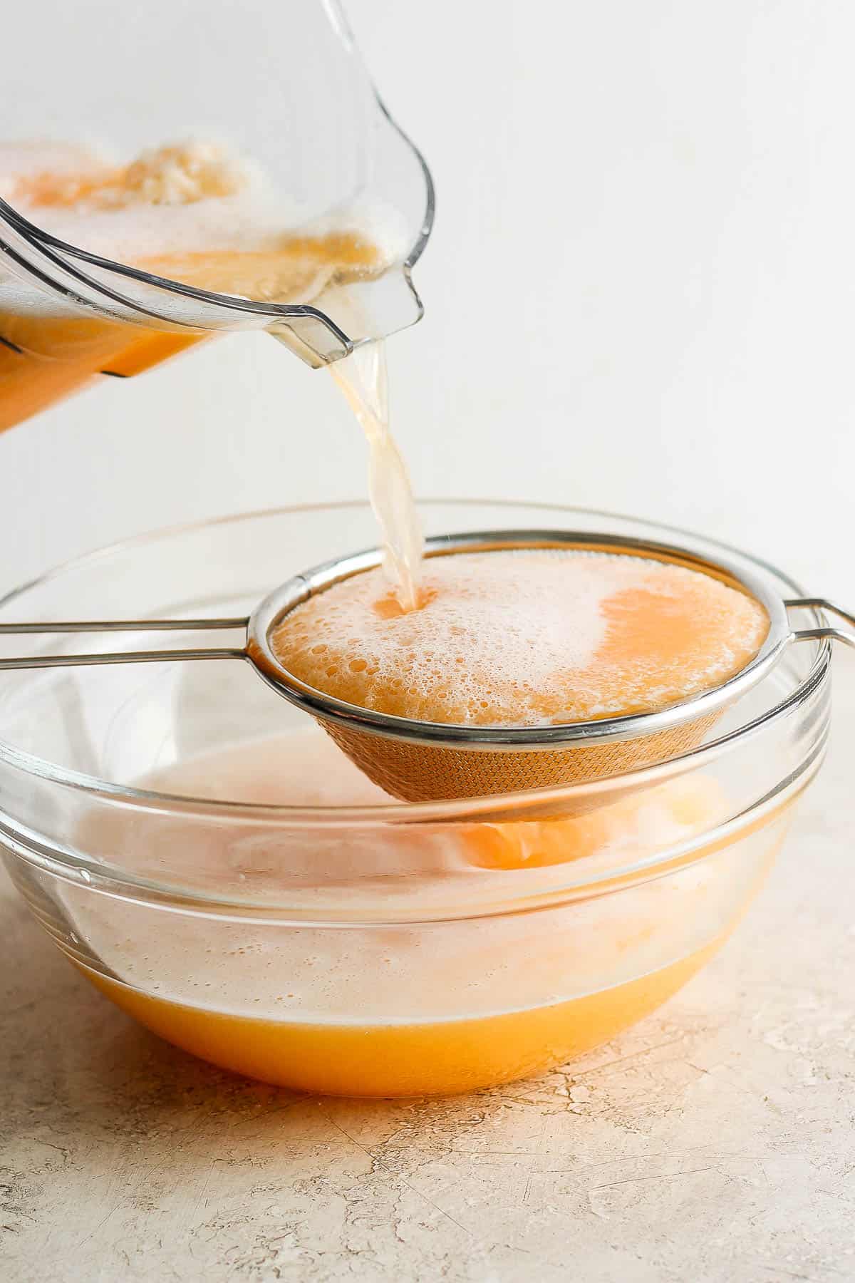 Agua de melon being poured through a strainer.