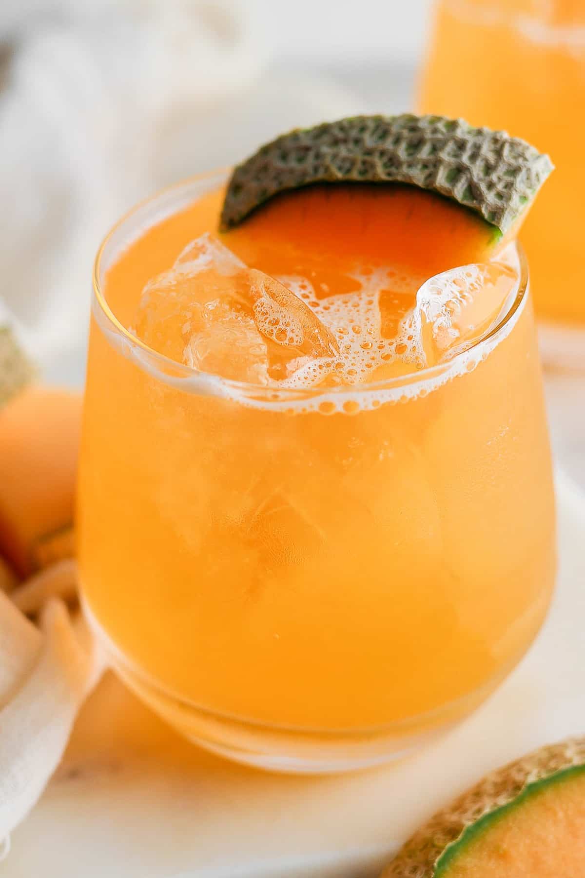 Agua de melon in a glass with ice and garnished with a cantaloupe wedge.