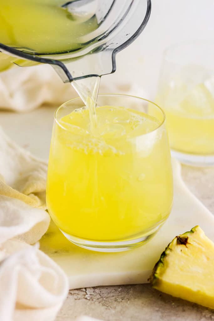 Agua de pina being poured into a glass with ice.